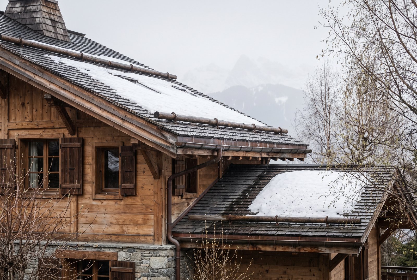 Chalet en bois traditionnel à Megève en intersaison, avec neige fondante sur le toit et gouttières, illustrant l'entretien hors saison
