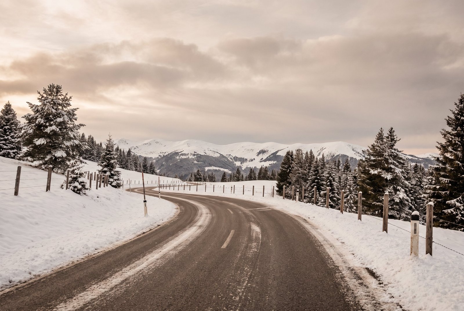 Route de montagne alpine enneigée et sinueuse, illustrant le trajet vers Megève en hiver